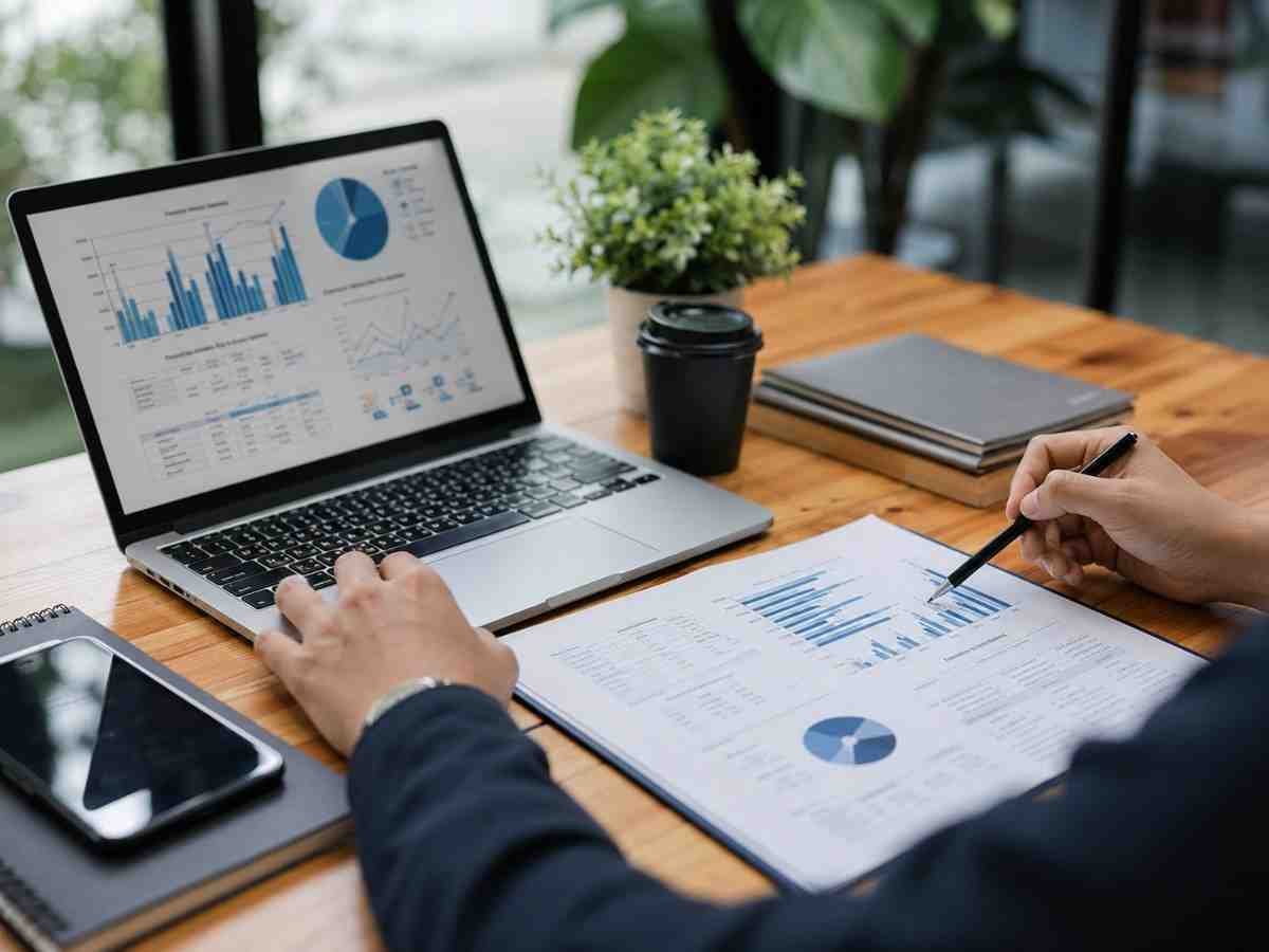 Person reviewing SaaS SEO performance charts on a laptop and printed reports in a modern office workspace.